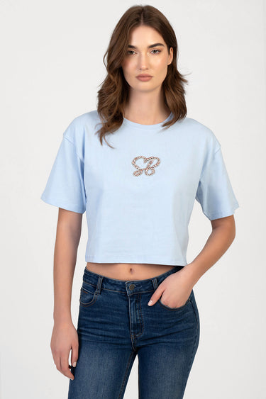 woman wearing a light blue cropped boxy short sleeve t shirt with a bejeweled logo on the chest