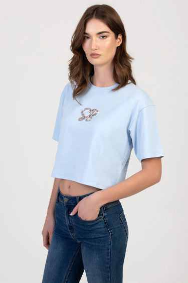 woman in light blue cropped t shirt with a rhinestone emblem on the chest and dark blue jeans