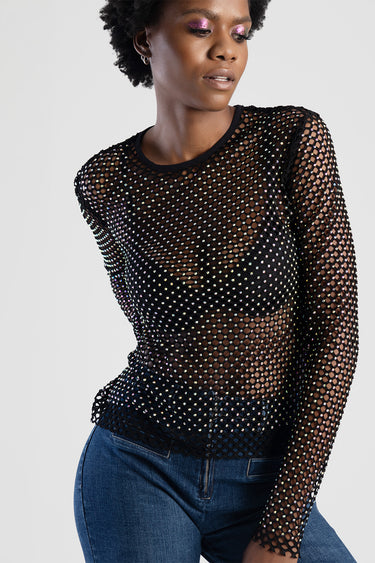 woman wearing a black rhinestone mesh top over a dark bralette, paired with blue denim jeans