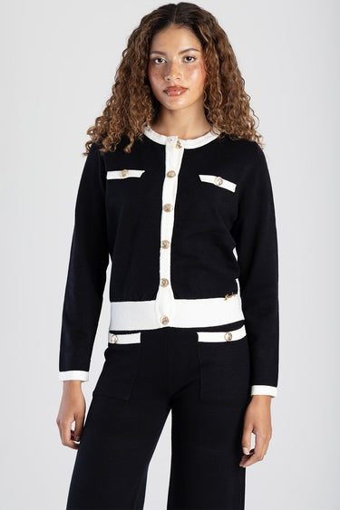 woman wearing a black knit cardigan with white trim and gold buttons, paired with matching black pants