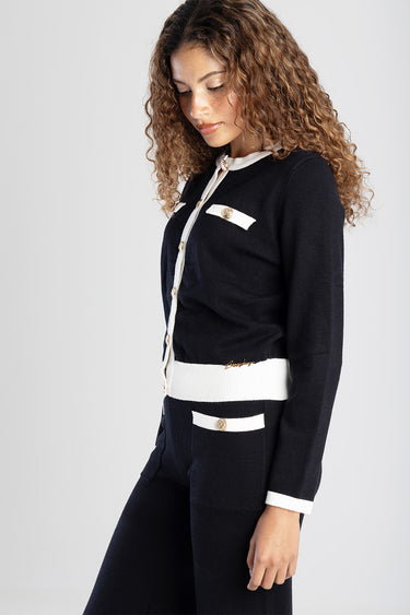 woman wearing navy knit cardigan with white trim, gold buttons, and white pocket accents