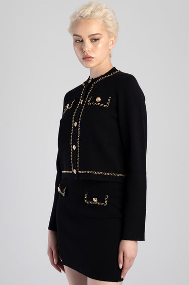 woman in black knit cardigan with gold chain trim and gold buttons, matching gold trimmed pockets