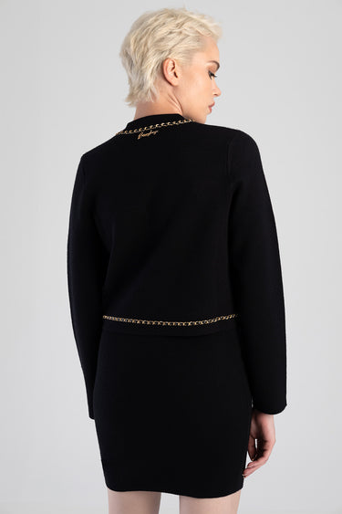 black knit cardigan with gold chain trim at the neckline and hem, worn by a model, back view