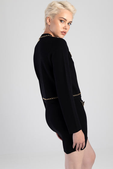 side view of a model wearing a black knit cardigan with gold chain trim and belt accents