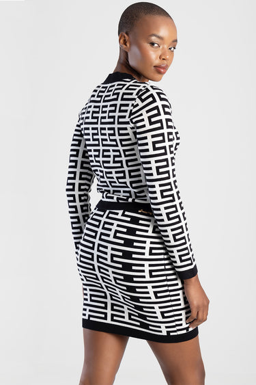 woman wearing a black and white geometric knit cardigan dress with long sleeves and a black waistband and hem, back view