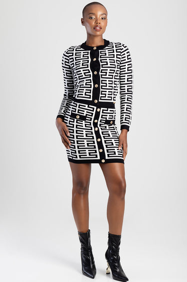 woman in a black and white geometric knit cardigan with a matching mini skirt and gold buttons