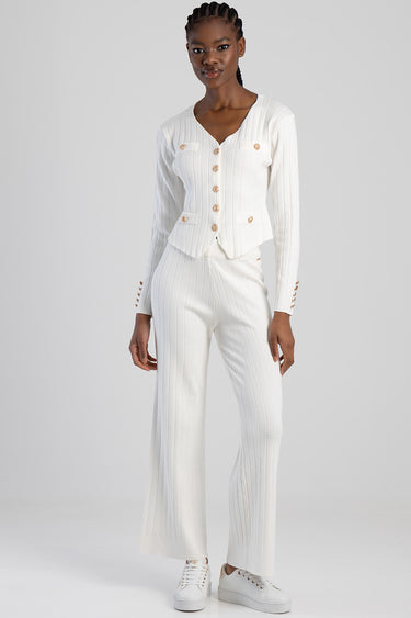 woman in a white ribbed knit cardigan with gold buttons and pocket flaps, paired with matching ribbed knit trousers and