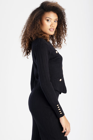 side profile of a woman in a black ribbed knit cardigan with gold buttons and a matching skirt
