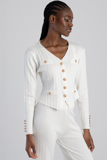 woman wearing a white knitted cardigan with a v neck, gold buttons, and matching ribbed knitted pants