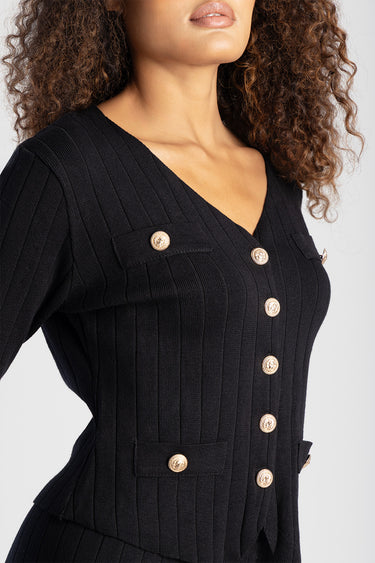 woman wearing a black ribbed knit cardigan with gold buttons, v neck and pocket flaps