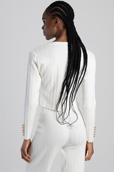 back view of white ribbed knit cardigan with gold button cuffs, paired with matching pants; model with long braids