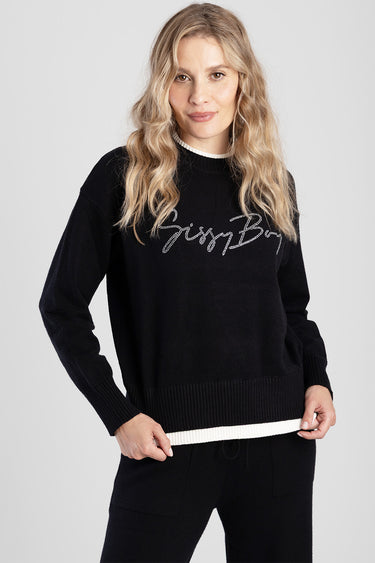 woman wearing a black knit pullover with white trim at the neckline and hem, rhinestone script across the chest