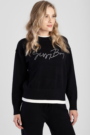 woman in black knit pullover with white ribbed hem and neckline; script lettering on chest.