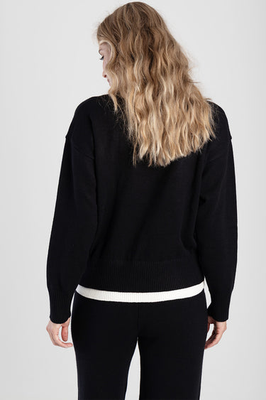 back view of a black knit sweater with a white striped hem and wavy blonde hair