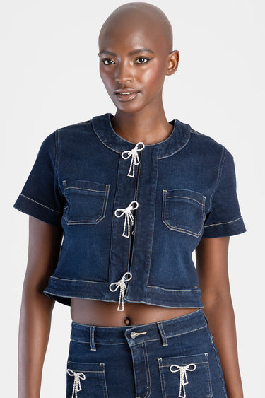 woman wearing a dark blue denim top with short sleeves, round neckline, three rope ties down the front, and chest pockets