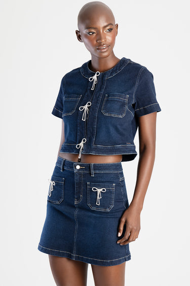 woman wearing a dark blue denim cropped top with rope ties and a matching denim skirt with pockets and bow accents