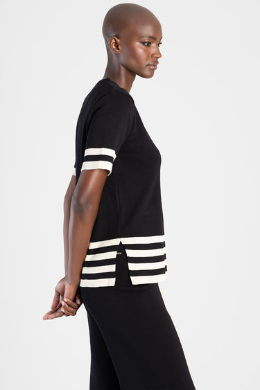 black knit short sleeve top with white striped cuffs and hem and side slits, model in profile