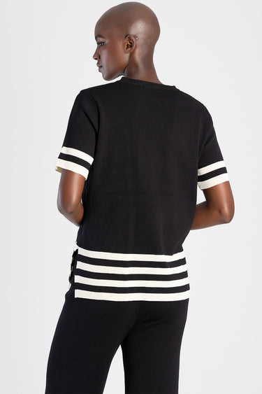 back view of a black knit short sleeve top with white stripes on the sleeves and hem, paired with black pants