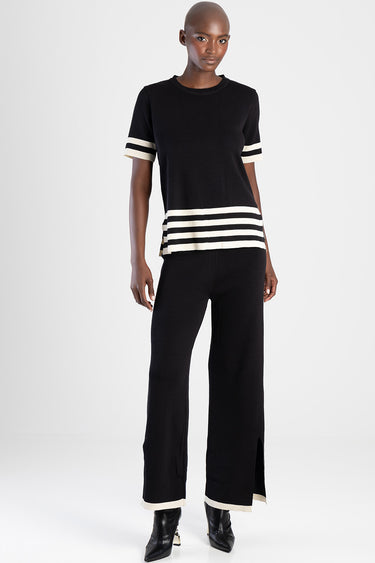 woman wearing a black knit top with white stripes on the cuffs and hem, paired with black wide leg pants with white trim at