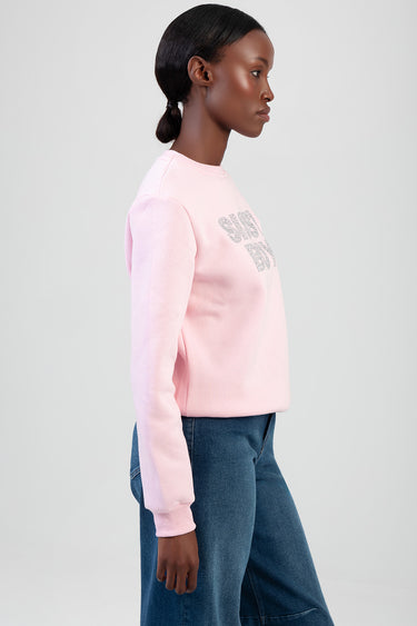 side view of a woman wearing a pale pink sweatshirt with glittery lettering and blue denim jeans
