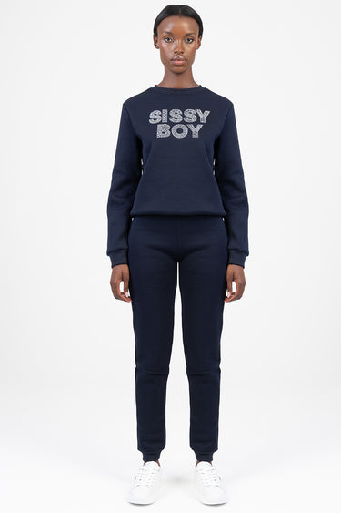 model wearing navy blue sweatshirt and matching jogger pants with white sneakers; the top has a glittery logo reading sissy