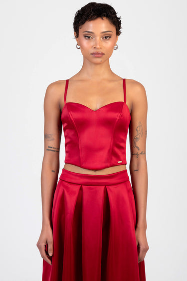 model wearing red satin corset top with thin straps and a matching pleated red skirt