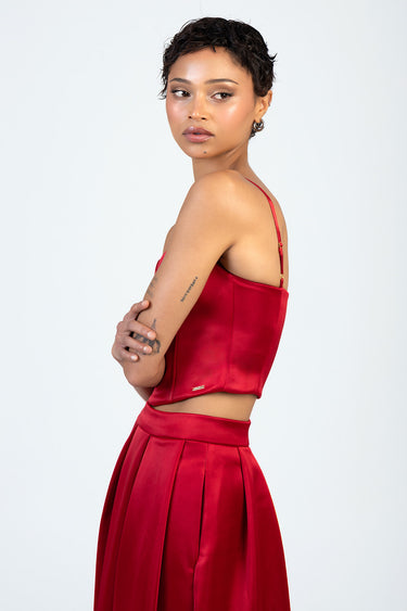 profile of a woman with short dark hair wearing a red satin corset top with thin straps and a matching pleated high waist