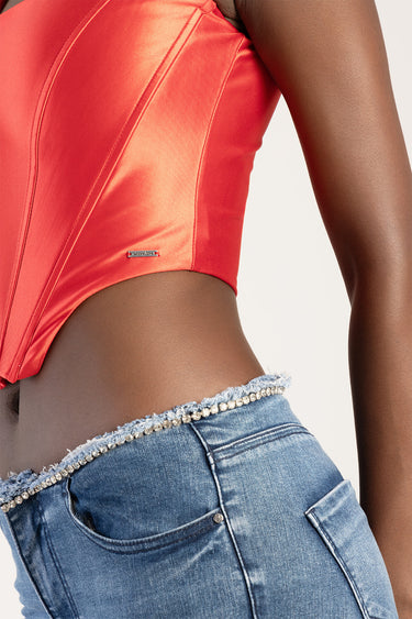side view of red satin corset top with visible seams and a small metal badge, paired with blue jeans trimmed with