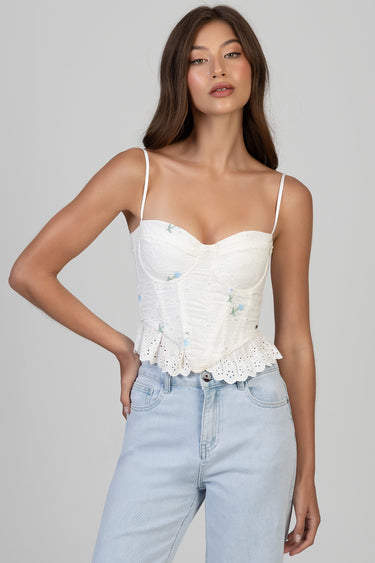 woman wearing white lace corset top with spaghetti straps and a ruffled hem, paired with light wash jeans
