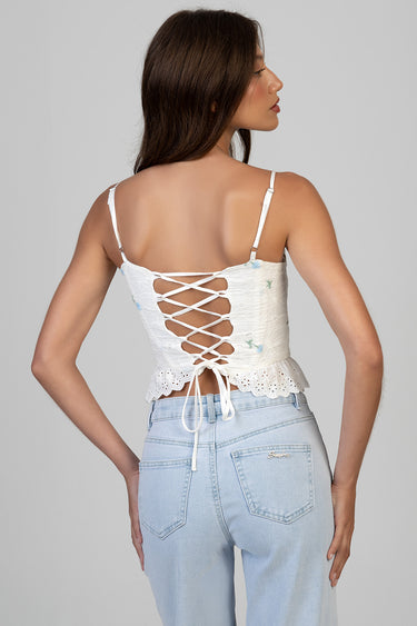woman wearing white lace corset top with crisscross back lacing and scalloped hem, paired with light wash jeans