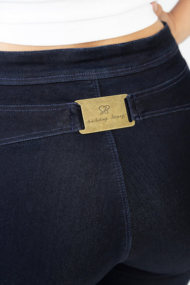 close up of dark indigo denim jeans at waist with belt loop and brass plaque engraved with sissy boy