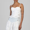 woman in a white embroidered peplum top with scalloped hem and a tiered eyelet skirt with light blue denim waistband