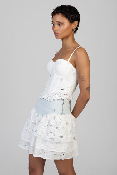 side view of a woman in a white lace top and light blue tiered lace skirt with a denim waist panel