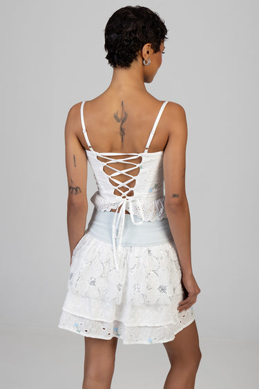 back view of a woman in a white lace top with a lace up back and a tiered eyelet lace mini skirt