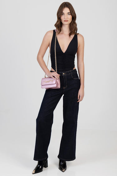 woman wearing a black ruched sleeveless top with dark wide leg jeans and black heeled boots, carrying a pink crossbody bag