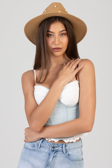 woman wearing a wide straw hat with pearl accents, white lace crop top and light wash denim jeans