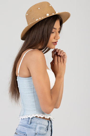 side profile of a woman wearing a pearl studded straw hat and a light blue denim corset top with lace trim