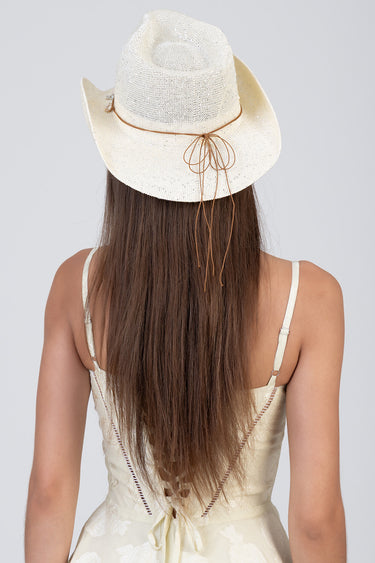 back view of a person wearing a straw western hat with a leather cord tied in a bow, long straight hair, and a pale dress