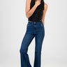 woman wearing blue flare leg jeans and a black sleeveless polka dot top with scalloped edges