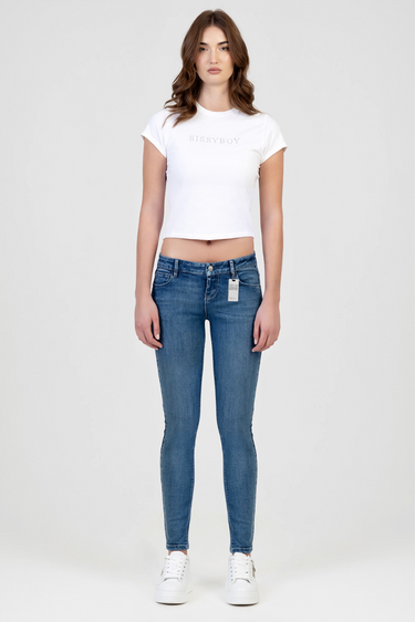 woman wearing a white short sleeve t shirt and blue super low waist skinny jeans standing against a light background