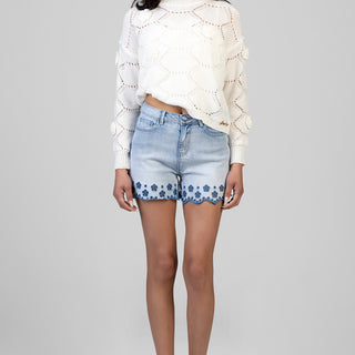 model wearing white knit sweater and light wash denim shorts with blue floral scalloped trim