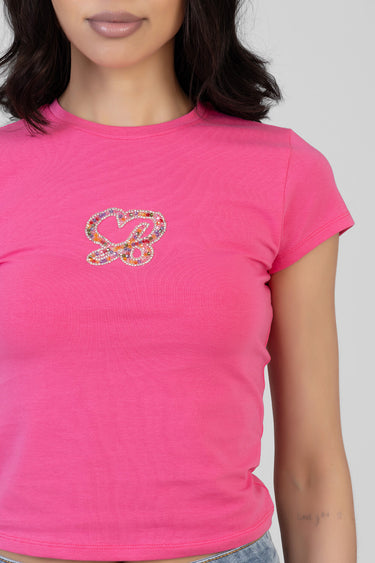 woman wearing a bright pink short sleeve t shirt with a rhinestone heart bow graphic on the chest