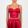 model wearing red satin corset top with thin straps and a matching pleated red skirt