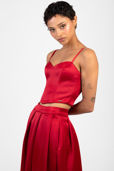 woman in a red satin corset top with thin straps paired with a matching high waisted pleated skirt
