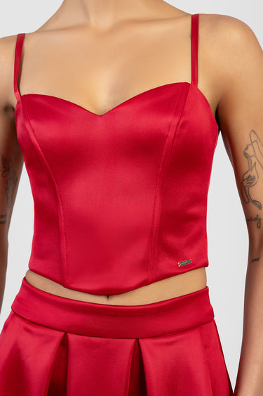 red satin corset top with thin straps and sweetheart neckline, fitted waist, with a matching satin skirt and a small gold