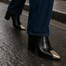 black leather ankle boots with a gold metal toe cap, paired with blue jeans