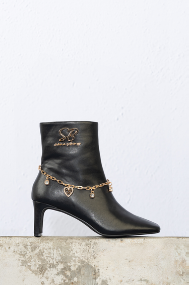 black leather ankle boot with a gold chain ankle bracelet and heart and jewel charms