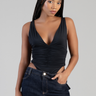 model wearing a black ruched deep V bodysuit with sleeveless straps, paired with dark wash jeans against a neutral backdrop.