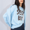 woman wearing a light blue knit sweater with a brown graphic text, paired with a matching cardigan and dark denim jeans